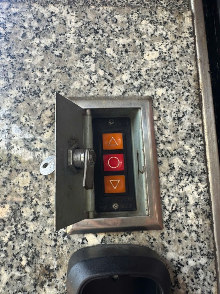 Hộp điều khiển cửa cuốn treo tường: mở khóa bằng chìa, kéo cánh kim loại để lộ ba nút điều khiển